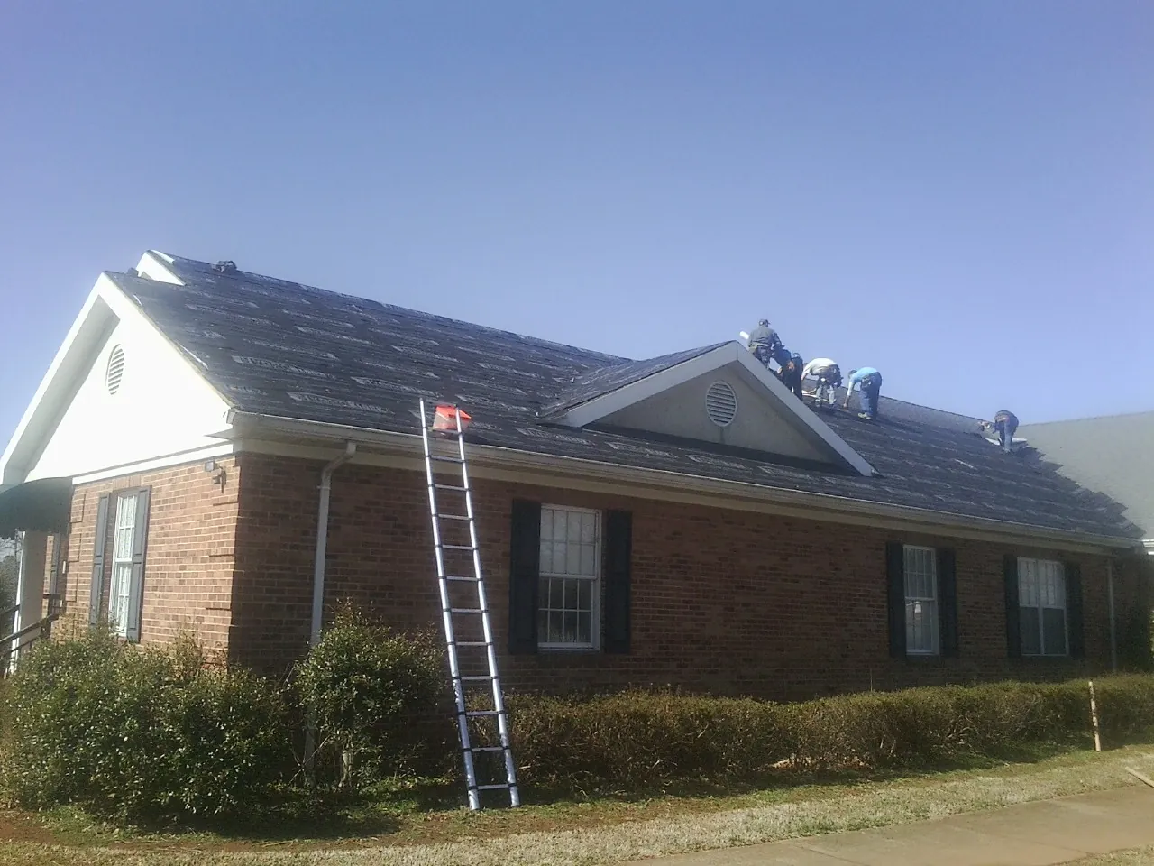 Crew tearing shingles off a brick ranch roof with a ladder set — Metal Roof Repair work by our crew in Hampton