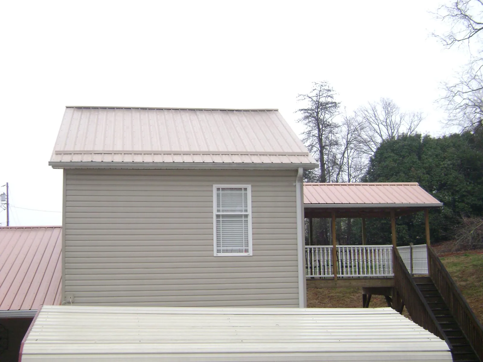 Tan metal roofs on a two story addition and attached porch, from a Roof Replacement job in Hampton